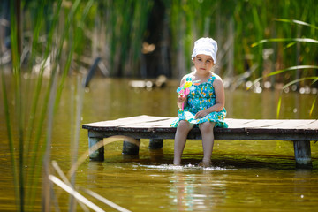 Girl barefoot sitting on the bridge near the lake. children with whirligig.
