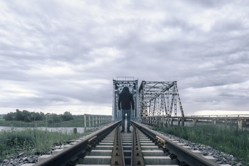 A man is standing on the old train bridge over a river.