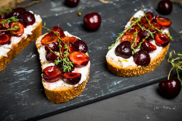 Bread with ricotta cheese and cherries on the wooden background. Shallow depth of field.
