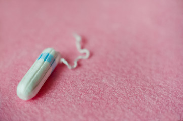 A female hygienic tampon with a blue border lies on a pink background. There is room for your text