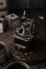 vintage offee grinder with two old cups of coffee with cocoa beans on dark brown surface opposite the chest of drawers. Still life. Coffee break
