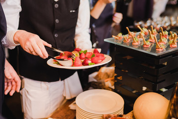 Catering banquet table at reception. Restaurant presentation, molecular gastronomy, haute cuisine, food consumption, party concept. Waiter serving strawberry.