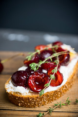 Bread with ricotta cheese and cherries on the wooden background. Shallow depth of field.