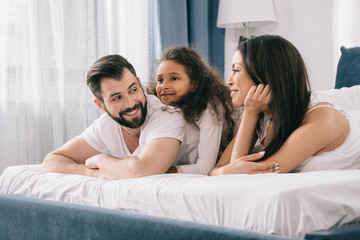 Happy multiethnic family with one child lying together in bed