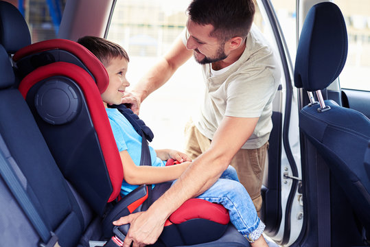 Small Son In Car Seat Being Put In Back Of Car By Father