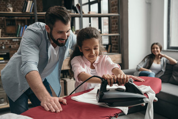 Fototapeta premium smiling father with little daughter ironing clothes at home