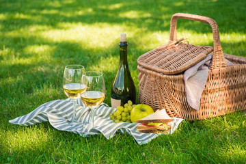 Close-up view of wicker picnic basket, sandwich, fruits and bottle of wine with glasses on napkin