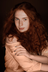 pretty tender redhead woman posing in beige clothes and looking at camera, isolated on black