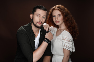 redhead girlfriend and bearded boyfriend posing for studio shot, isolated on brown