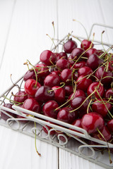 White metall basket with ripe red cherries on white wooden background. Summer berries
