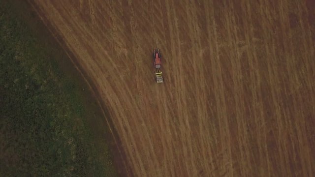 Aerial view of tractor making hay bale rolls in field after wheat harvest, drone pov