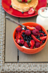 Healthy breakfast on garden furniture: cottage cheese with sour cream, strawberry, raspberry and blueberry, pancakes, yogurt and juice. Selective focus