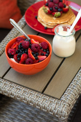 Healthy breakfast on garden furniture: cottage cheese with sour cream, strawberry, raspberry and blueberry, pancakes, yogurt and juice. Selective focus