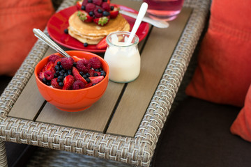 Healthy breakfast on garden furniture: cottage cheese with sour cream, strawberry, raspberry and blueberry, pancakes, yogurt and juice. Selective focus