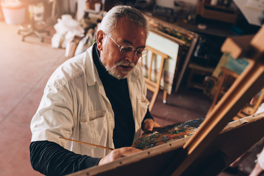 Old man artist painting oils in his studio.