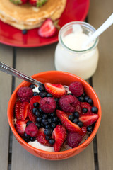 Healthy breakfast on garden furniture: cottage cheese with sour cream, strawberry, raspberry and blueberry, pancakes, yogurt and juice. Selective focus
