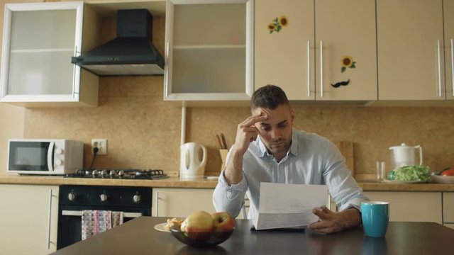 Uspet young man reading letter with unpaid bill in the kitchen at home