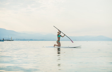 Fototapeta na wymiar Young beautiful slavian woman tourist practicing paddle boarding in sea at beach near ancient fortress wall and shipyard in city center of Alanya, Mediterranean Turkey