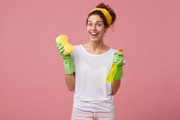 Indoor shot of beautiful housewife with yellow headband and white T-shirt holding mop and washing...