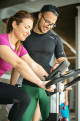 Fototapeta premium Young man exercising on stationary bikes in fitness class. Man workout in gym. Personal trainer monitors the speed