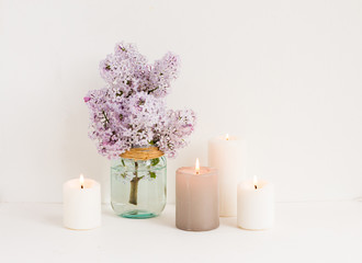 Fototapeta na wymiar Spa composition. White candles, towel, lilac flowers on white wooden background.