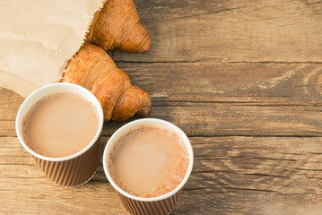 Tasty fresh croissants in paper beg and coffee in a paper cup on old wooden background.