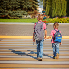 Two boys with backpack walking, holding on warm day on the road.