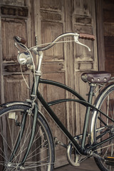 Fototapeta na wymiar vintage bicycle on vintage wooden house. vintage tone. Thai style vintage wooden door not Wood stain. the door made of Teak wood (Tectona grandis) is Auspicious Tree in Thailand