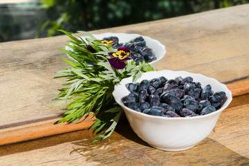 White plate with ripe honeysuckle berries with a sprig of grass with the reflection in the mirror on the old wooden table