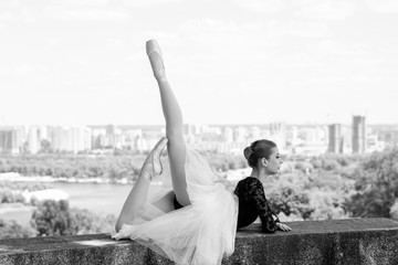 Young beautiful ballerina dancing against a background of city panorama in the park 