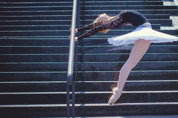 Young ballerina in ballet costume dancing in city park, on stairs feeling breath of big city life and freedom