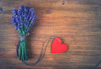 Fototapeta premium Bouquet of lavender flowers and red wooden heart on a old wooden background. Photo in vintage style