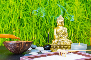 Buddha, incense stick, candle, rake, sand and zen stones as zen garden background