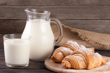 jug and glass of milk with croissants on a wooden background