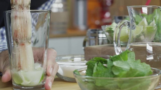 A bartender uses a piece of sugar cane to muddle limes in a cocktail glass. Shot with a RED Dragon digital cinema camera.