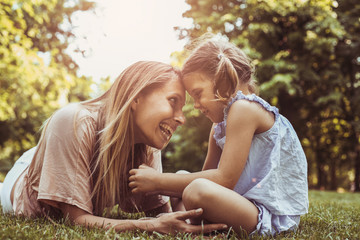 Fototapeta premium Mother and daughter sitting together on green grass. Mother and daughter having funny conversation.