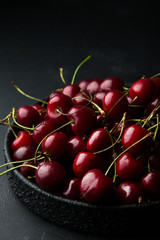 Red ripe cherries on black textured plate standing on black concrete background. Space for text. Summer fruits and berries