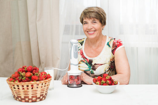 Happy senior female preparing fresh strawberry berries for making smoothie in the kitchen..