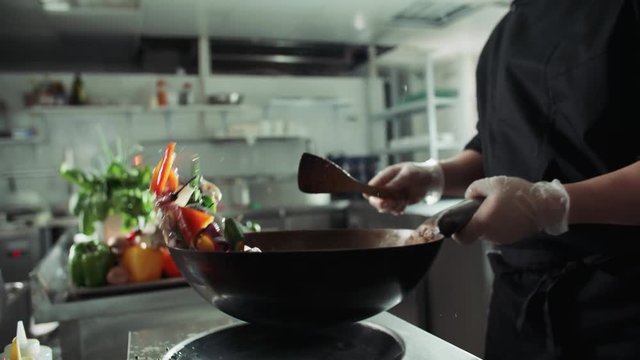 Asian chef works coloured mixed roasting vegetables in the wok with flame , kitchen Asian restaurant, slow motion