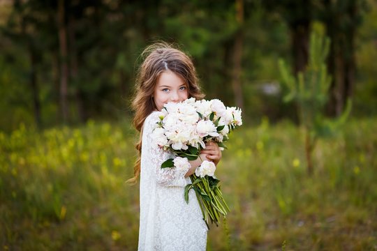 Little Girl Six Years Old With Brown Hair And Blue Eyes With A Bouquet Of Peony Flowers Wearung White Dress, Smiling