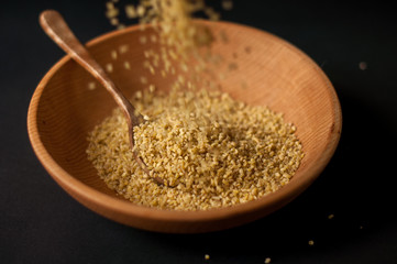 Dry bulgur wheat in brown wooden bowl isolated on dark wood