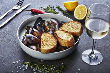 mussels in white wine sauce with glass of white wine white bread toasts, decorated with hilly pepper, lemon and sea salt