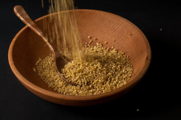 Dry bulgur wheat in brown wooden bowl isolated on dark wood