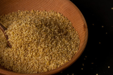 Dry bulgur wheat in brown wooden bowl isolated on dark wood