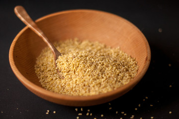 Dry bulgur wheat in brown wooden bowl isolated on dark wood