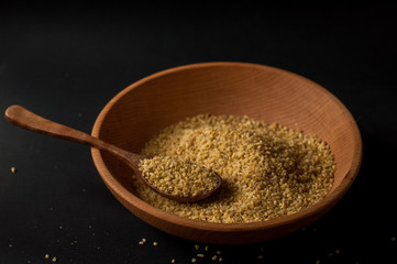 Dry bulgur wheat in brown wooden bowl isolated on dark wood