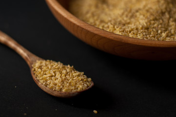 Dry bulgur wheat in brown wooden bowl isolated on dark wood