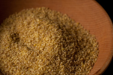 Dry bulgur wheat in brown wooden bowl isolated on dark wood