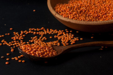 Heap of red lentils in a wooden bowl on dark background