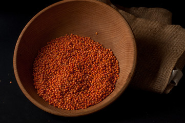 Heap of red lentils in a wooden bowl on dark background